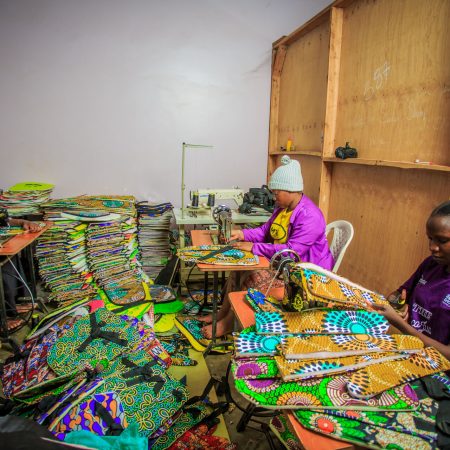 Women artisans at Smart Girls Uganda sewing Ecojua Smart Bags made from recycled plastic waste, combining solar-powered lighting and reusable menstrual kits to empower girls and promote sustainability.